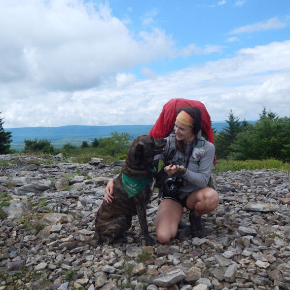 Maya backpacking at the crest of Dolly Sods kneeling and holding hands with her dog, Ace.